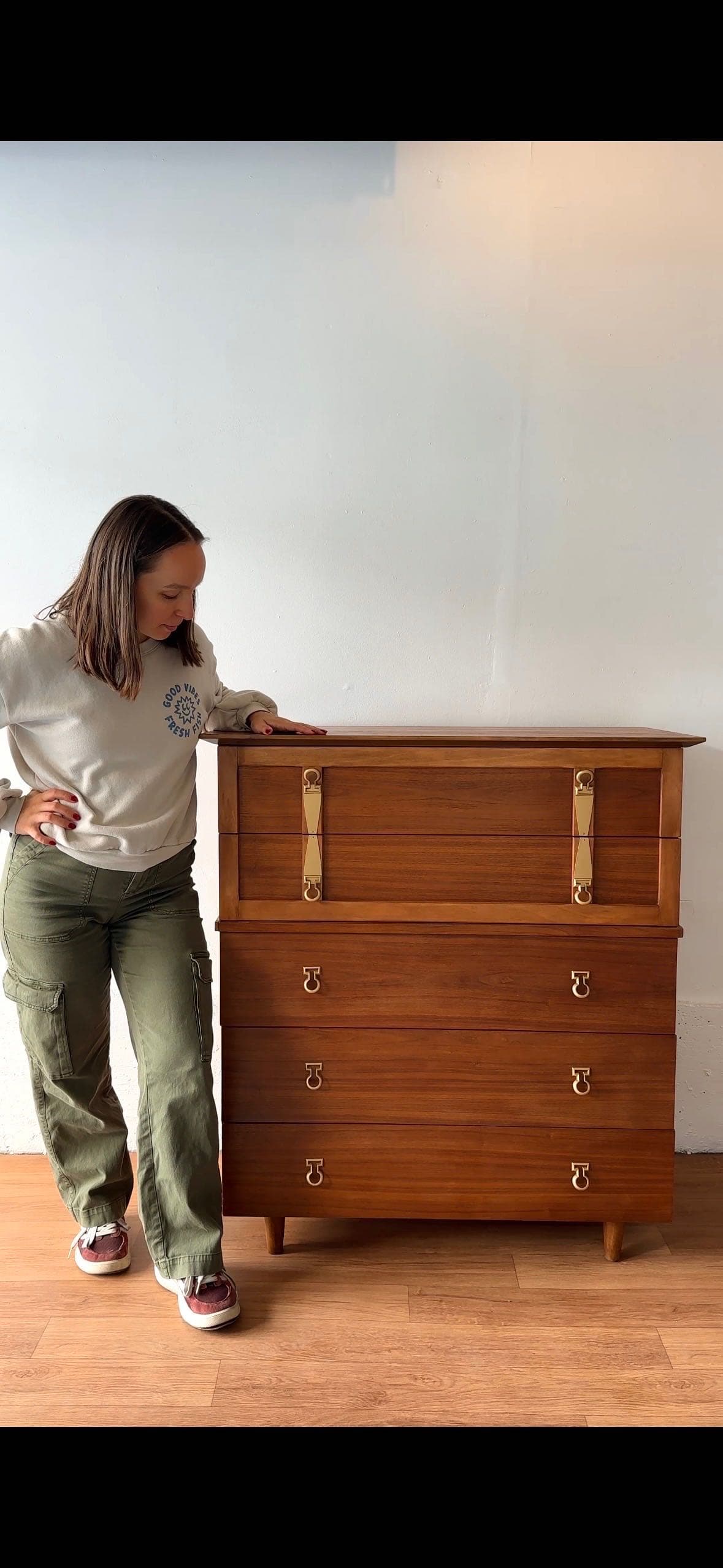 Bridget looking down at a recently refinished mid-century modern dresser